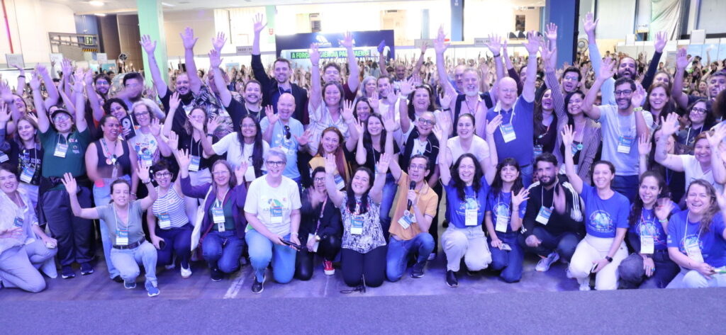 Está imagem mostra um grupo de pessoas de diversas idades reunidos no evento de abertura da FECCI 2025. Na imagem, as pessoas posam para a foto com as mãos levantadas e sorriem.